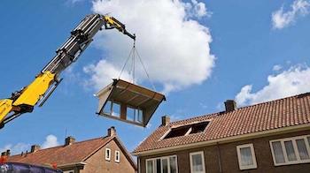 A crane moves a section of house into place