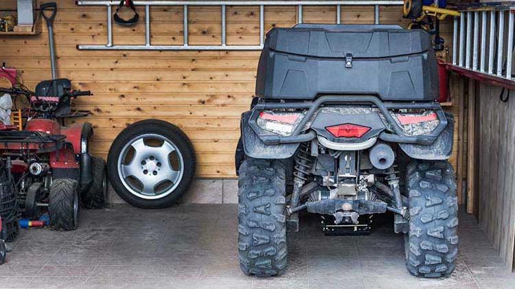 An ATV is parked in a garage next to a tire.