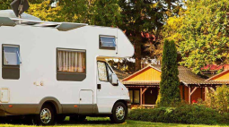 A motorhome parked outside a brick house with a tree in the front yard.